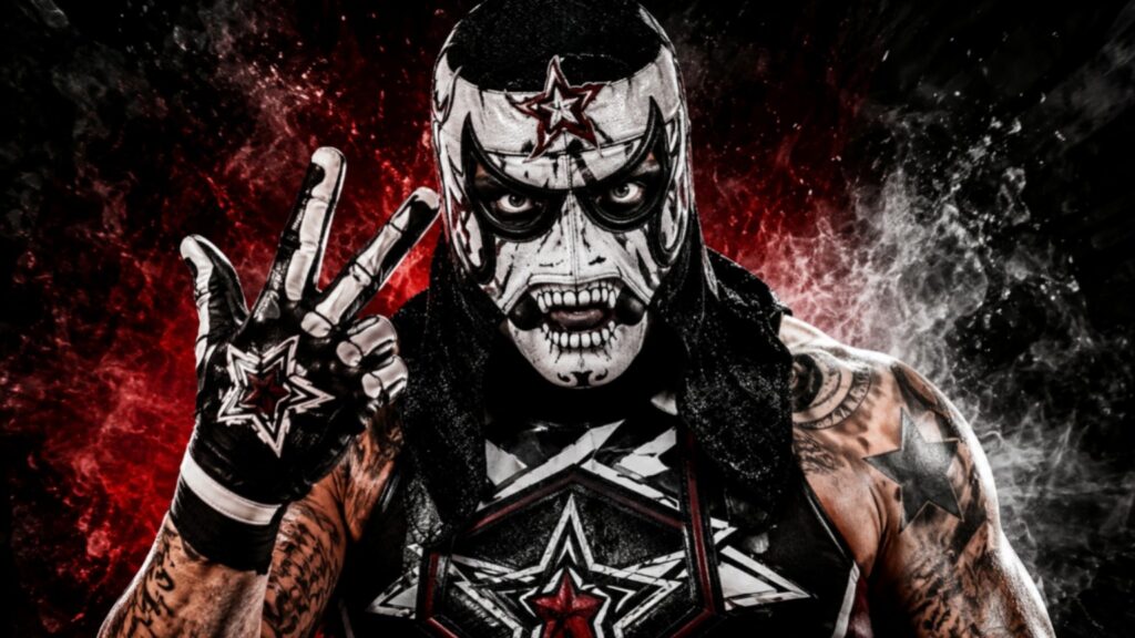 Pentagón Jr. strikes his signature hand gesture in a dramatic close-up, wearing his iconic black-and-white lucha mask with an intense red-and-black smoky background.