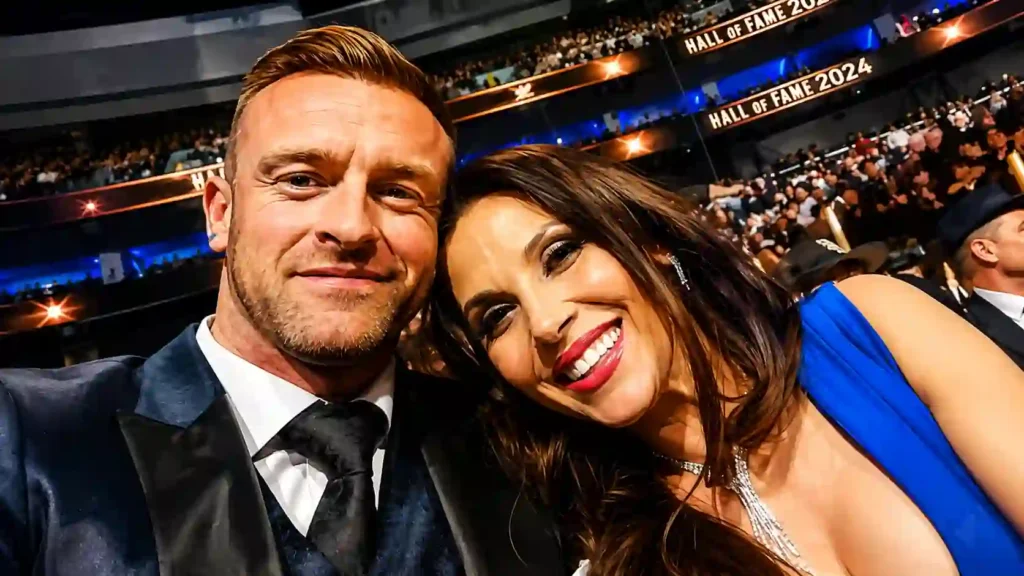 Nick Aldis and his wife sharing a selfie at the WWE Hall of Fame ceremony inside a packed arena.